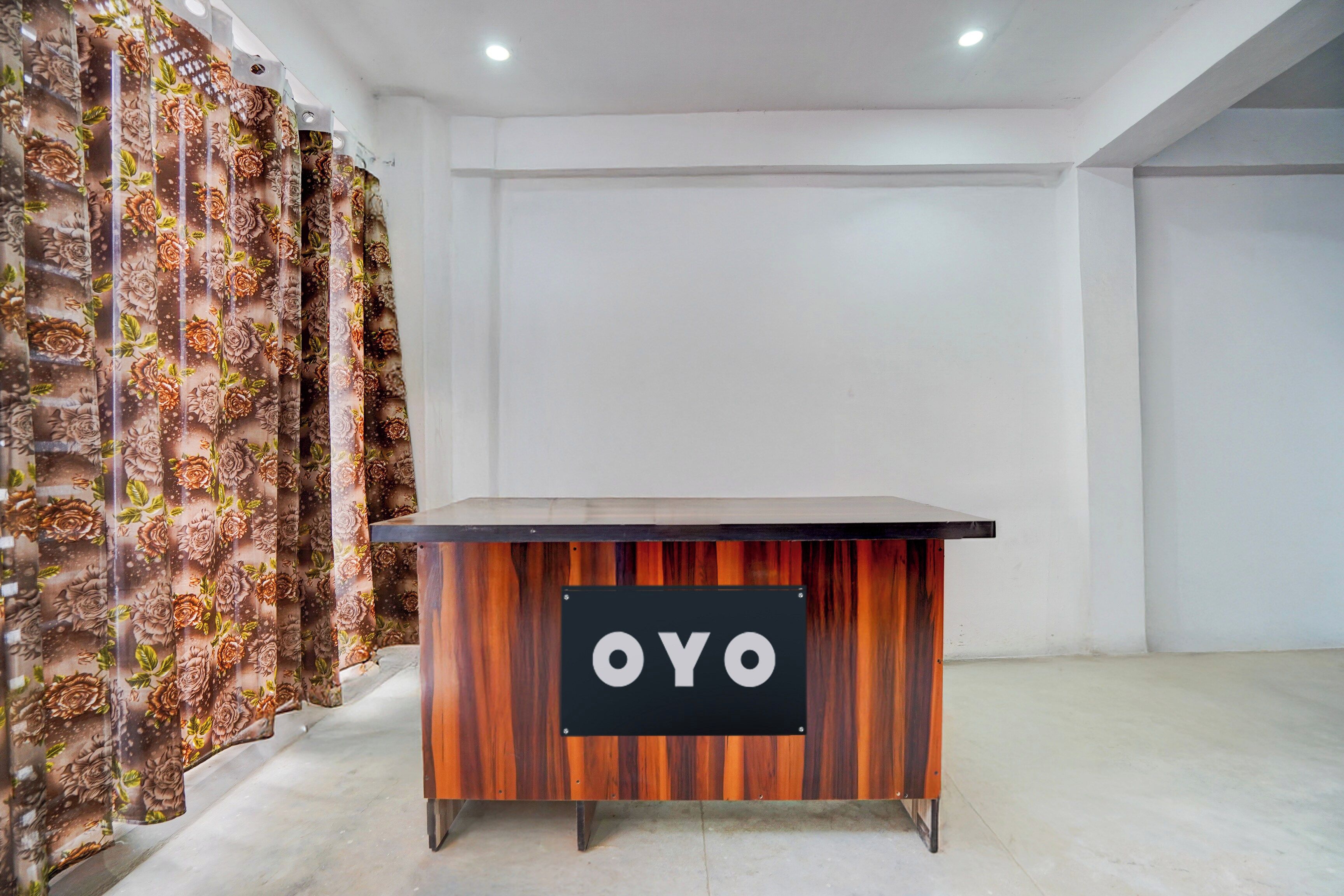 Una recepción con un letrero que dice 'OYO' en un interior moderno con paredes lisas y una cortina estampada.