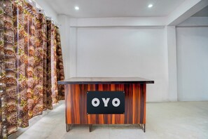 Balcão de recepção com uma placa indicando 'OYO', em um interior moderno com paredes lisas e cortina estampada.