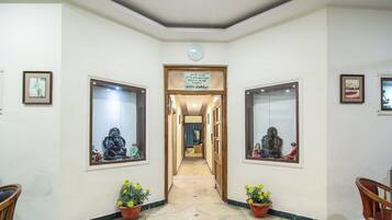 A hallway with framed artwork on the walls, potted plants, and a clock on the ceiling.