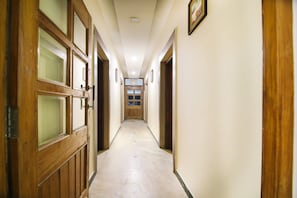 Un pasillo con puertas de madera y suelo de baldosas, que conduce a una habitación con ventana.
