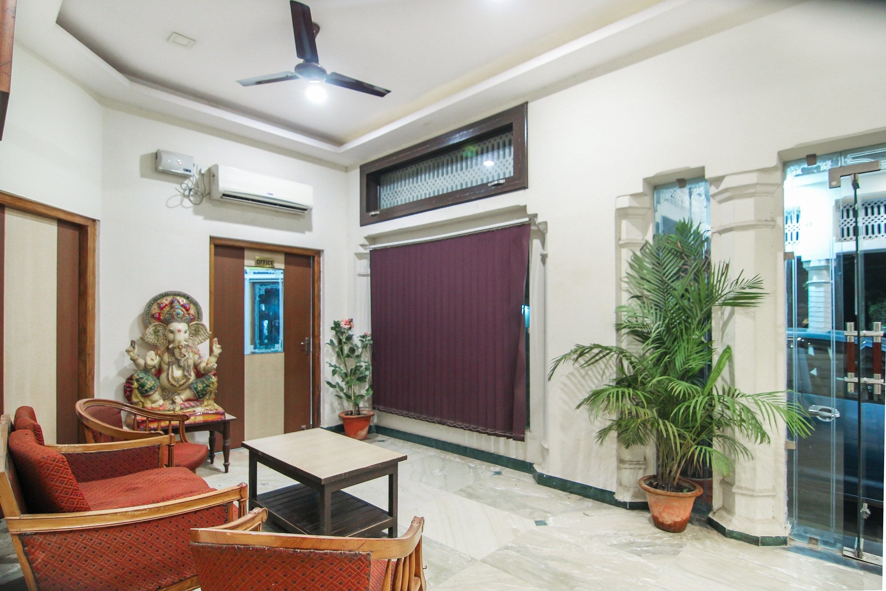 A hotel lobby with a ceiling fan, a statue, a reception desk, and a large potted plant.