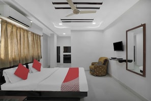 A hotel room with a bed, a chair, a television, and a ceiling fan. - Hotel O Rudra Palace (Ahmedabad)