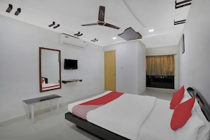 A bedroom with a bed, a television, a bench, an air conditioning unit, and a ceiling fan. - Hotel O Rudra Palace (Ahmedabad)