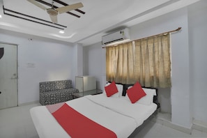A hotel room with a bed, a sofa, a wardrobe, an air conditioning unit, and a ceiling fan. - Hotel O Rudra Palace (Ahmedabad)