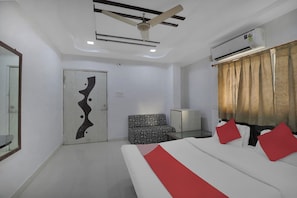 A hotel room with a bed, a chair, a wardrobe, a ceiling fan, and an air conditioning unit. - Hotel O Rudra Palace (Ahmedabad)