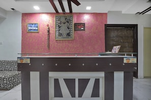 A reception desk with a digital clock, framed artwork, and a sign indicating the hotel name. - Hotel O Rudra Palace (Ahmedabad)