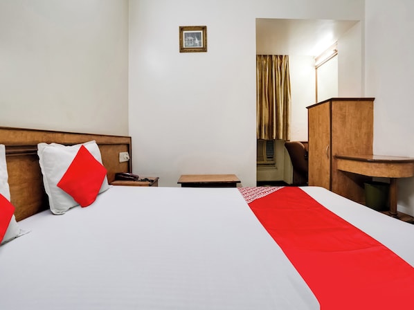 A hotel room with a large bed, a wooden headboard, a bedside table, a desk, and a chair. - Hotel O Raj Palace (Ahmedabad)