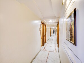A hotel corridor with wooden doors, a marble floor, and a framed picture on the wall. - Hotel O Raj Palace (Ahmedabad)