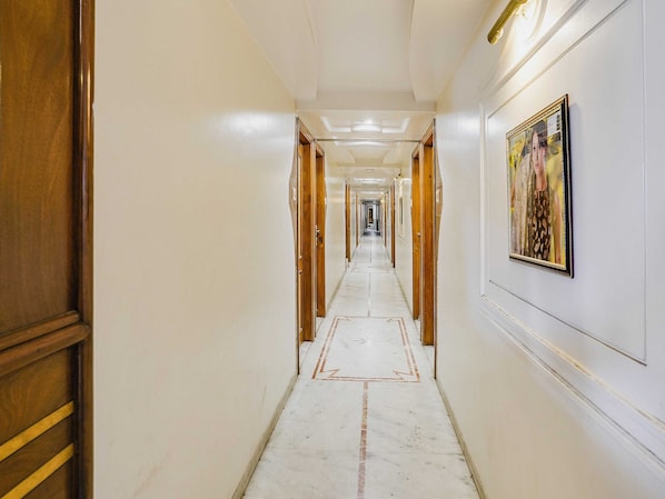 Un pasillo de hotel con puertas de madera, suelo de mármol y un cuadro enmarcado en la pared.