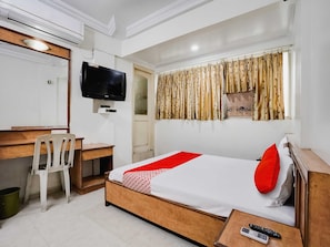 A hotel room with a bed, a desk, a chair, a television, and a window with curtains. - Hotel O Raj Palace (Ahmedabad)