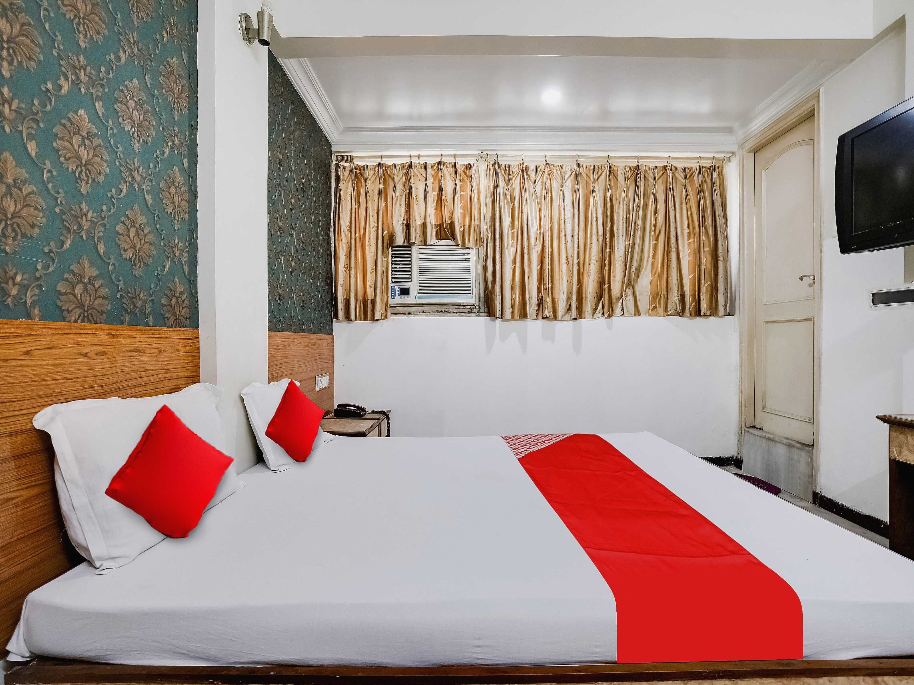 A hotel room with a large bed, a bedside table with a phone, a TV on the wall, and a window with curtains.