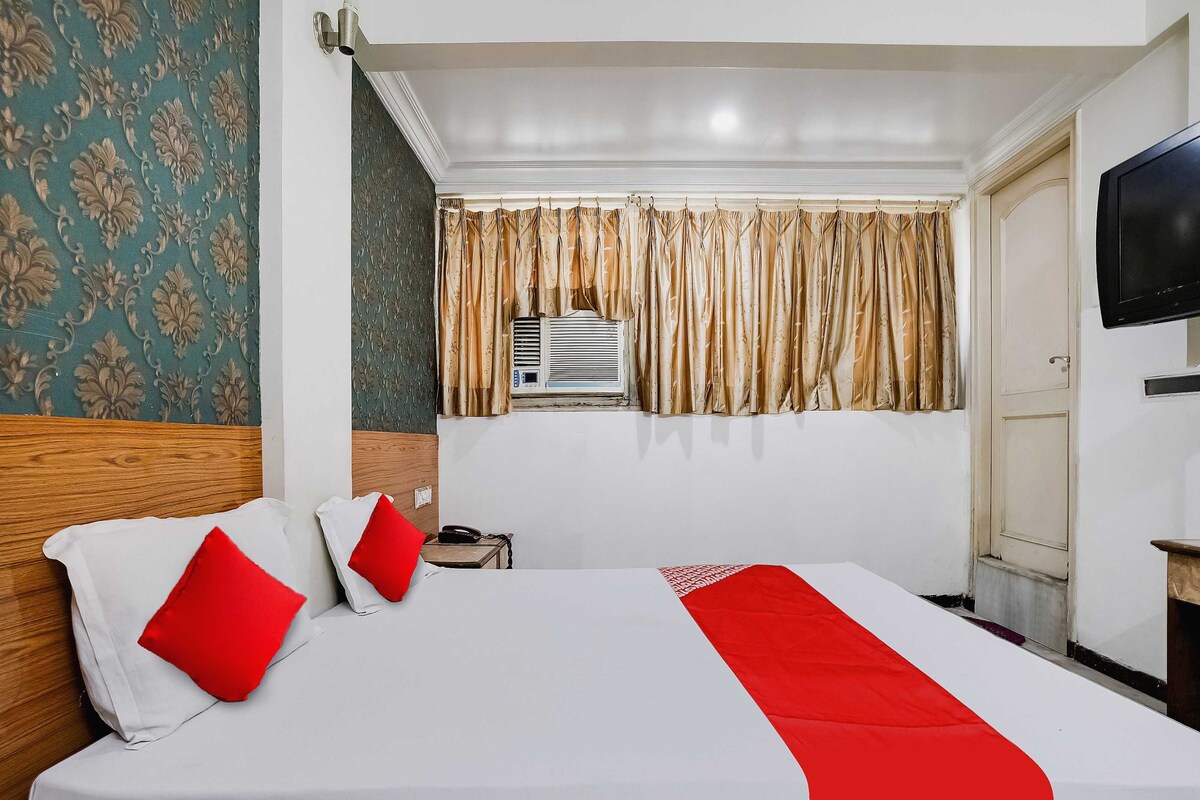 A hotel room with a large bed, a bedside table with a phone, a TV on the wall, and a window with curtains.