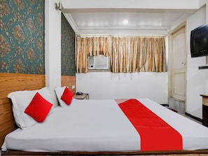 A hotel room with a large bed, a bedside table with a phone, a TV on the wall, and a window with curtains. - Hotel O Raj Palace (Ahmedabad)