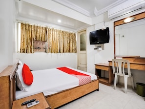 Habitación de hotel con cama, escritorio, silla, televisor y aire acondicionado.