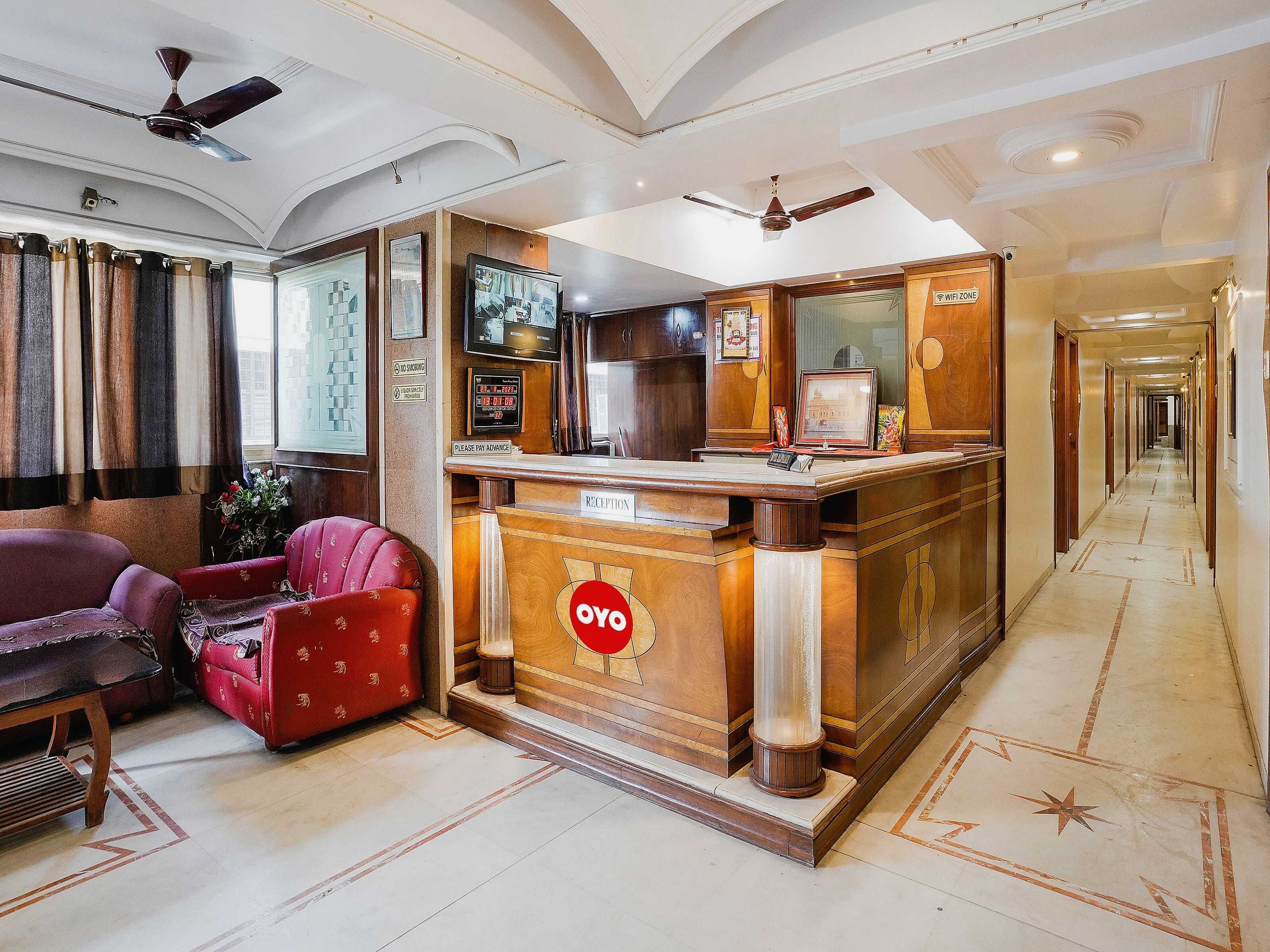 A reception area with a reception desk, a red sofa, a wooden chair, and a ceiling fan.