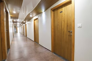 A long, narrow hallway with wooden doors and a tiled floor. - Hotel O Madhav Villa (Ahmedabad)