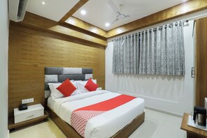 Habitación de hotel con cama, mesita de noche y ventana con cortinas estampadas.