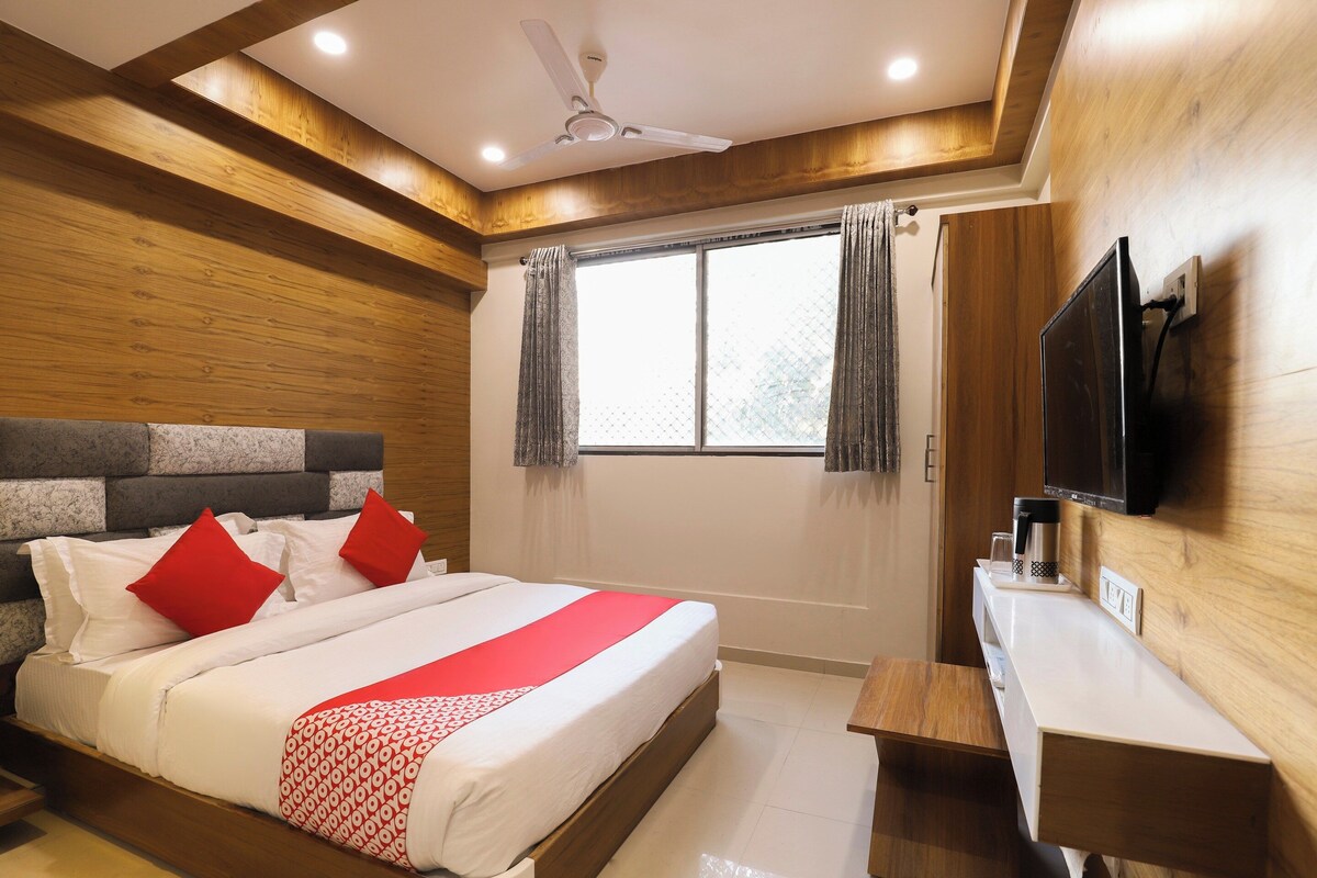 Habitación de hotel con cama, televisor montado en la pared, ventana con cortinas y ventilador de techo.