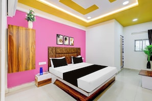 A bedroom with a bed, bedside tables, a wooden headboard, a pink wall, and a ceiling with recessed lighting. - Hotel O by OYO Shaligram (Ahmedabad)