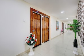 Pasillo de hotel con puertas de madera numeradas 102 y 103, un pedestal blanco con flores y una planta en maceta.