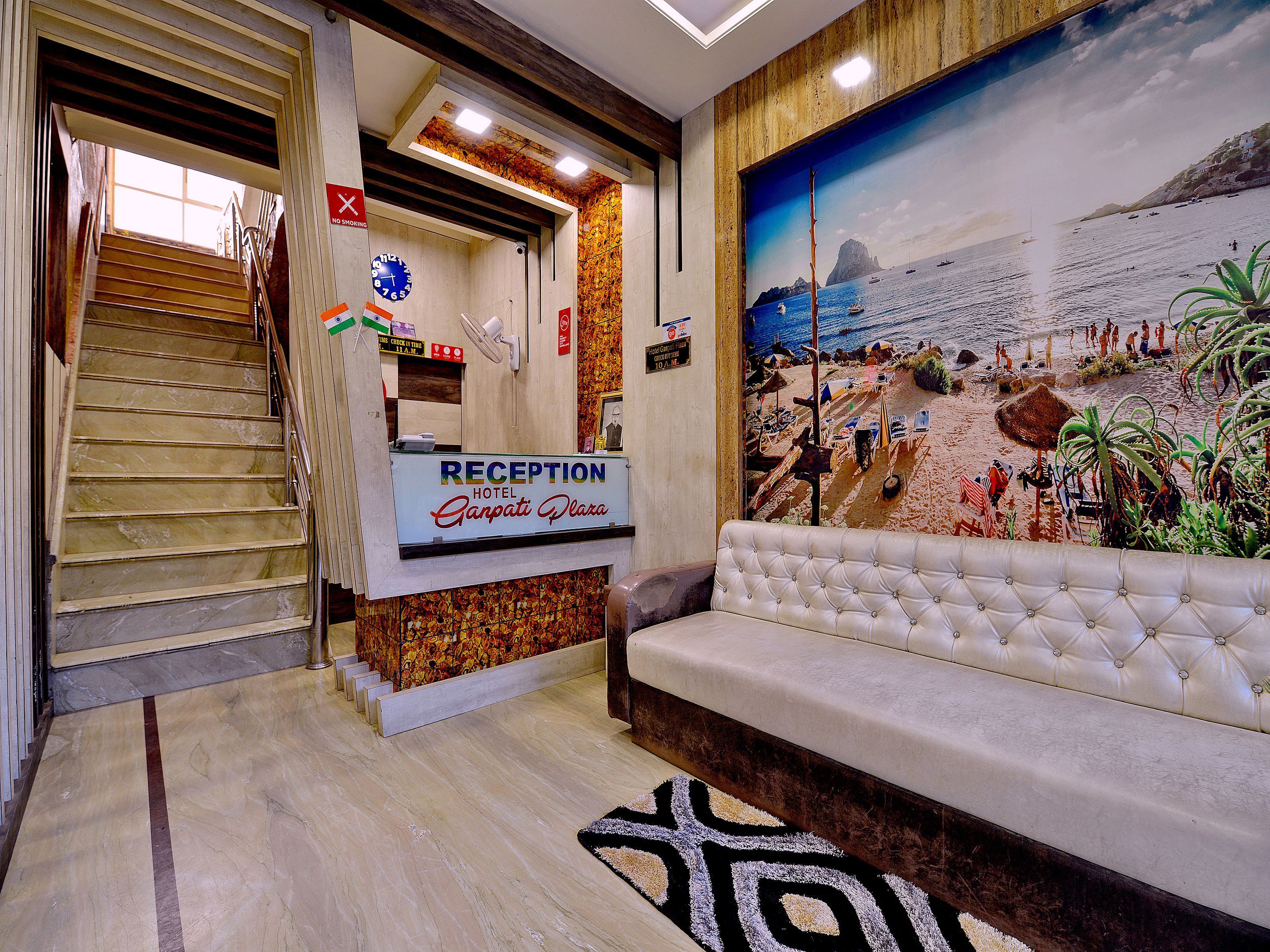 Una recepción con un cartel que dice 'Ganpati Plaza Hotel', una escalera y un mural de una escena playera.