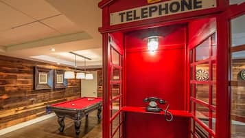 Ein Billardtisch und eine rote Telefonzelle in einem Raum mit Holzwänden und einer Decke mit eingelassener Beleuchtung.