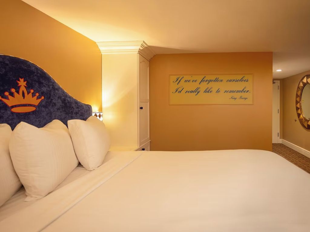 A hotel room with a bed, a decorative wall with a crown symbol, and a motivational quote.