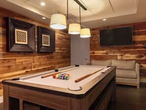 Una mesa de billar con bolas, un sofá e iluminación empotrada en una habitación con paneles de madera.