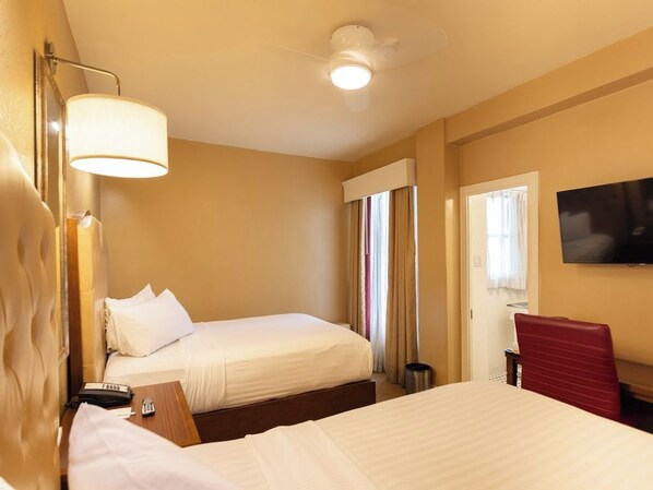 Ein Hotelzimmer mit zwei Betten, einem Fernseher, einem Schreibtisch und einem Sessel.