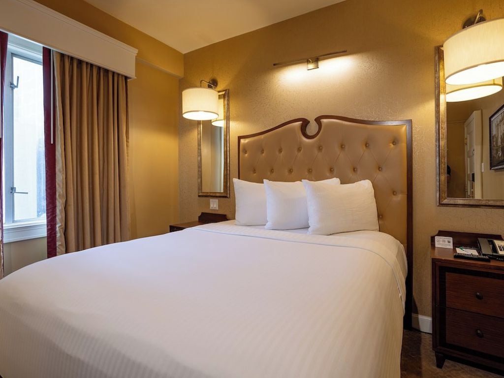 A hotel room with a large bed, a nightstand, a lamp, and a mirror.