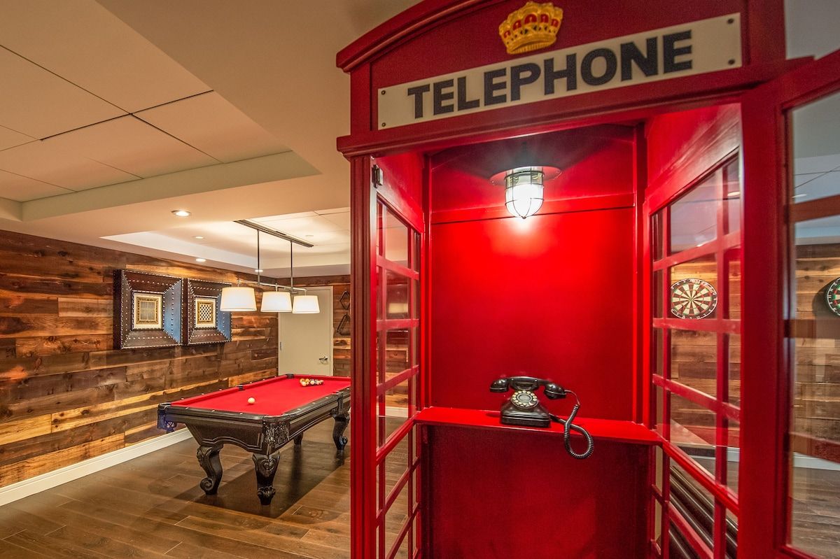 A billiards table and a red telephone booth in a room with wooden walls and a ceiling with recessed lighting.