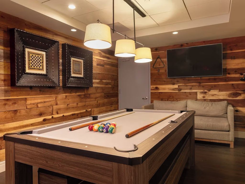 Ein Billardtisch mit Kugeln, eine Couch und Wandleuchten in einem Raum mit Holzvertäfelung.