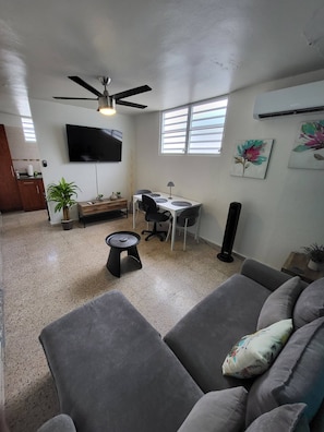 A living room with a sofa, a coffee table, a TV, a desk with a chair, and a ceiling fan.