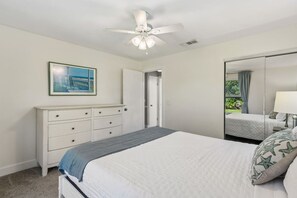 A bedroom with a bed, a dresser, a ceiling fan, a painting, and a mirror. - Aqua Oasis · Private Pool Bungalow, Fenced Yard (Jacksonville)