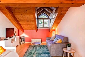 A cozy loft-style living room with a sloped ceiling, a sofa, a small coffee table, and a TV. - Wine Loft in the Center of Monforte d'Alba (Monforte d'Alba)