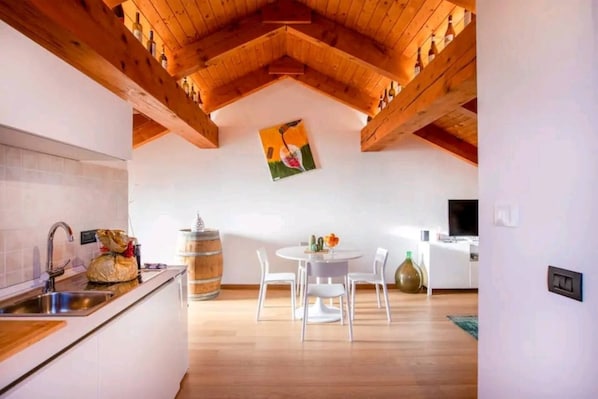 A kitchen with a wooden ceiling, a dining area with a table and chairs, and a kitchen counter with a sink and a bag of groceries. - Wine Loft in the Center of Monforte d'Alba (Monforte d'Alba)