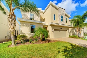 A modern two-story house with a stone facade, a garage, and a well-maintained lawn with palm trees. - 9BR pool & spa | Train bunks + Donkey Kong games (Kissimmee)