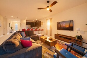 A modern living room with a sofa, coffee table, and TV. - 9BR pool & spa | Train bunks + Donkey Kong games (Kissimmee)