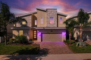 A two-story house with a stone facade, a garage, and a driveway. - 9BR pool & spa | Train bunks + Donkey Kong games (Kissimmee)