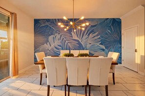 A dining area with a table set for four, a modern chandelier, and a large wall mural. - 9BR pool & spa | Train bunks + Donkey Kong games (Kissimmee)