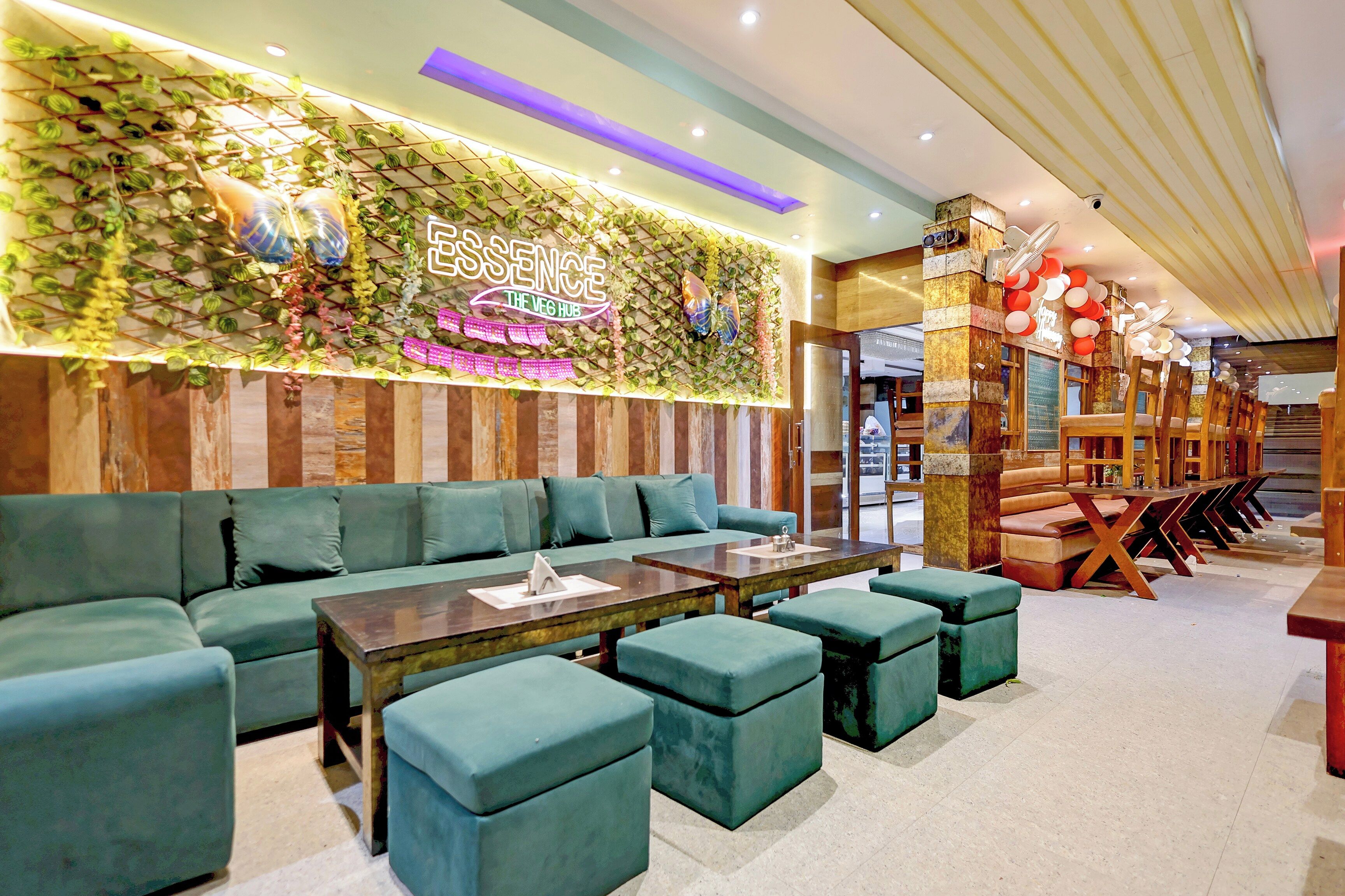 A restaurant interior with a green-themed wall, a neon sign, and a seating area with green upholstered sofas and tables.