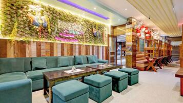 A restaurant interior with a green-themed wall, a neon sign, and a seating area with green upholstered sofas and tables.