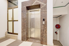 An elevator with a digital display, a door with a glass panel, and a red fire alarm on the wall. - Hotel O Essence Inn (Prayagraj)