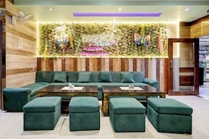 A modern lounge area with a green sofa, matching ottomans, and a wall-mounted sign reading 'ESSENCE THE VEG HUB'. - Hotel O Essence Inn (Prayagraj)
