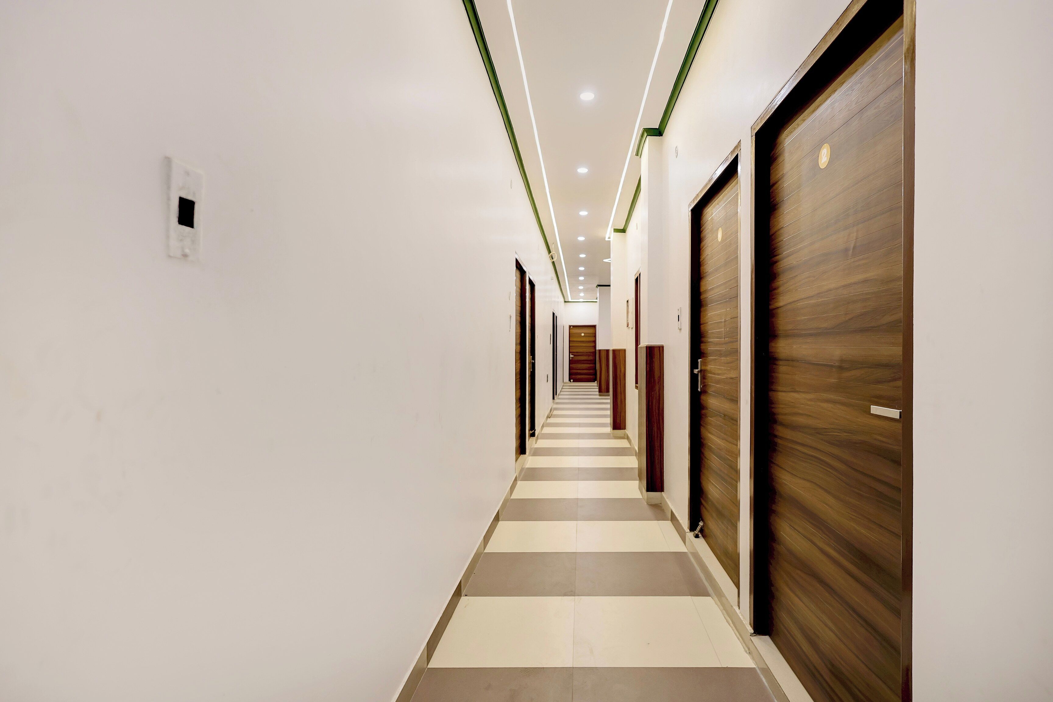 Un pasillo de hotel con piso de diseño ajedrezado, puertas de madera e iluminación empotrada.