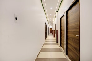 A hotel corridor with a checkered floor pattern, wooden doors, and recessed lighting. - Hotel O Essence Inn (Prayagraj)