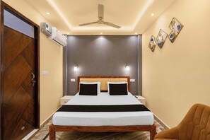Een hotelkamer met een bed, een houten deur, een airconditioning, een plafondventilator en wandlampen.