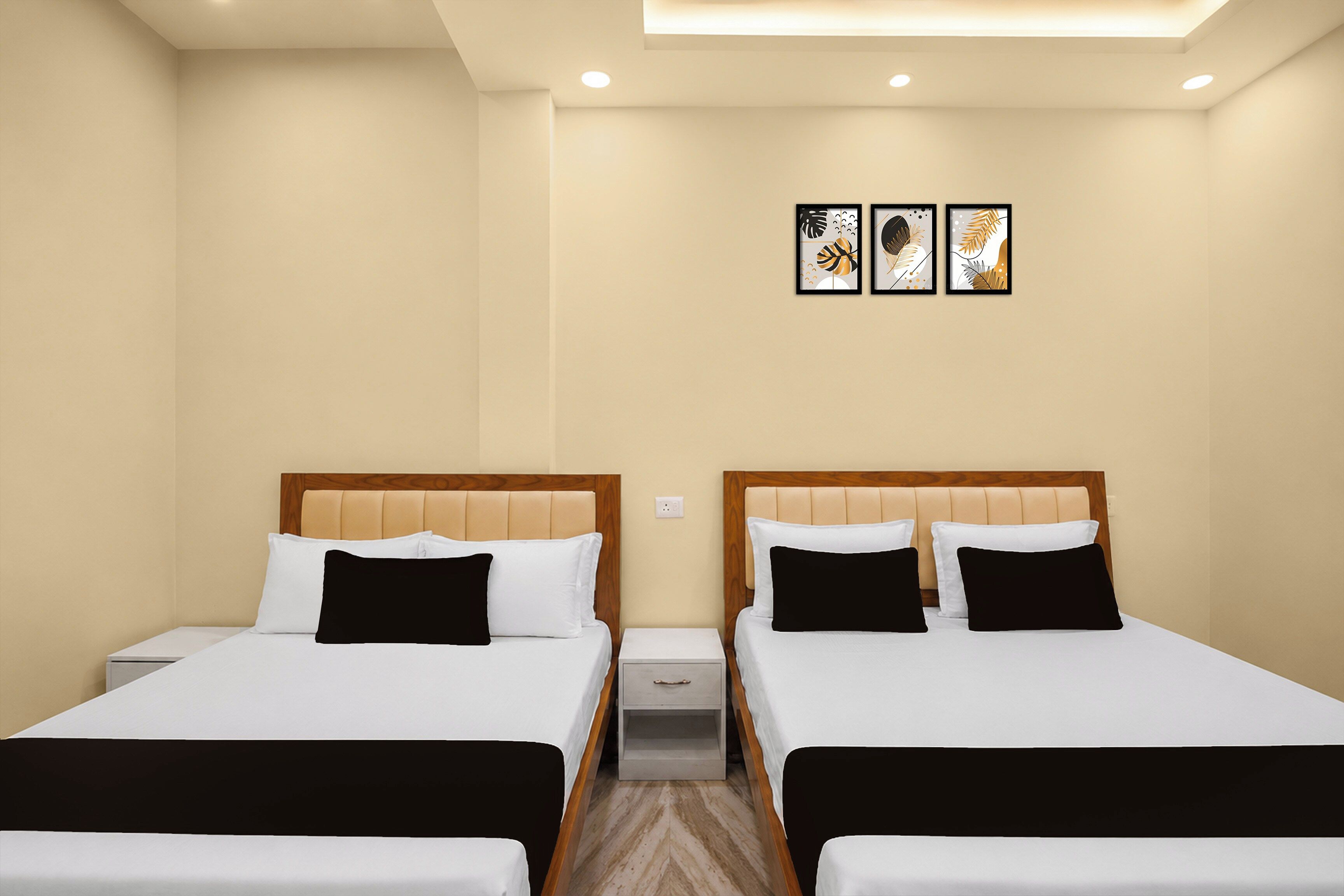 Habitación de hotel con dos camas, cada una con cabecero de madera y ropa de cama blanca. Hay tres cuadros enmarcados en la pared sobre las camas.