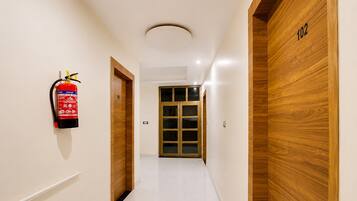 A hallway with a fire extinguisher mounted on the wall, wooden doors with numbers, and a glass door at the end.