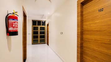 A hallway with a fire extinguisher mounted on the wall, a wooden door with the number 102, and a double door at the end.